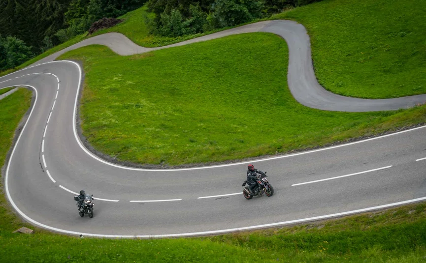 Two motorcycles on winding mountain road with green grass