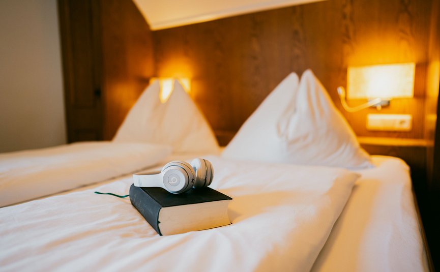 Kabelloser Kopfhörer auf einem Buch auf einem weißen Bett in gemütlichem Schlafzimmer