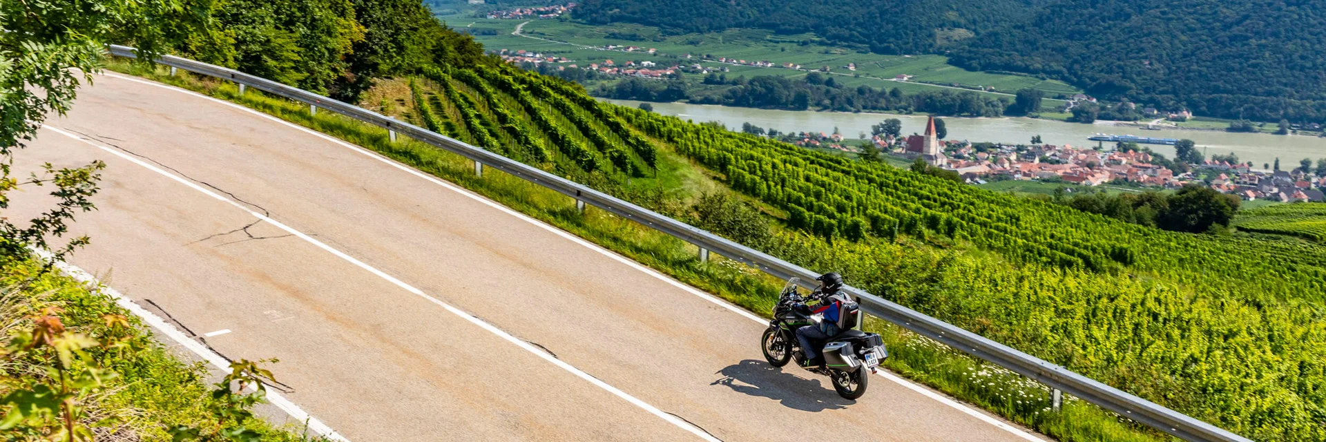 Motorcyclist riding on winding country road with vineyards and river view