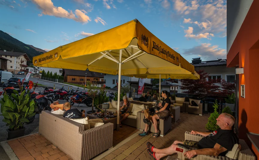 People sitting under yellow umbrella on terrace near parked motorcycles