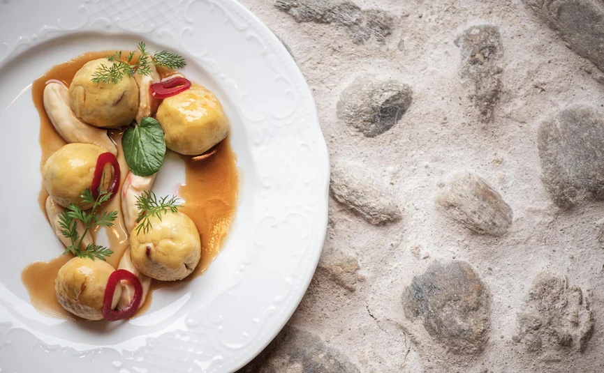 Five stuffed dumplings with sauce and garnish on a white plate