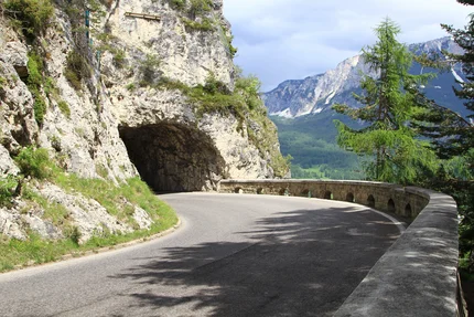 Winding mountain road with rock tunnel and view of forested mountains