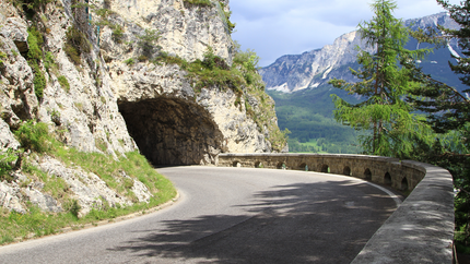 Kurvige Gebirgsstraße mit Felsentunnel und Ausblick auf bewaldete Berge