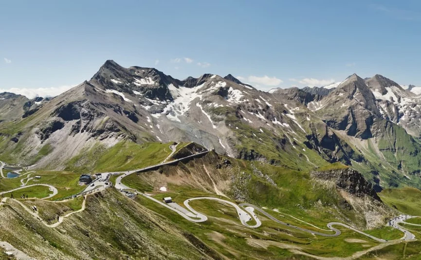 Bergpas met kronkelende weg en besneeuwde toppen in de zomer