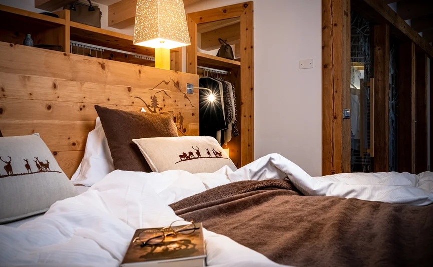 Cristallo Sport & Wellness Hotel **** © Andrea Acler Gemütliches Schlafzimmer mit Holzdekor, warmem Licht und Buch auf dem Bett