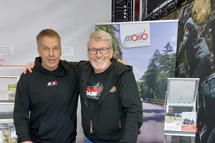 Two men at a MOHO Motorrad Hotels trade show booth