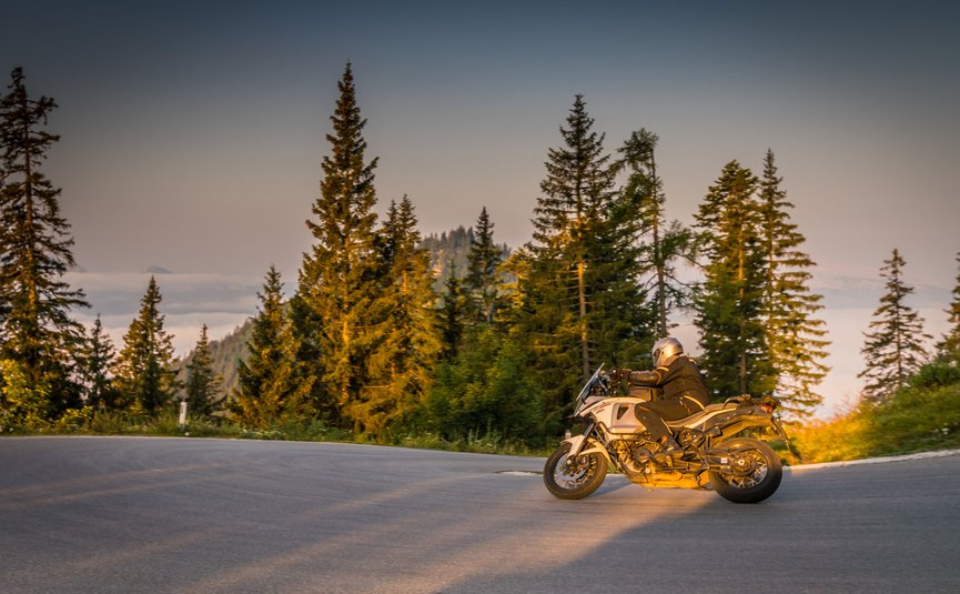 Almhotel & Genussgasthof Hierzegger ***S © Moppetfoto.de Motorradfahrer auf kurviger Straße vor Nadelbäumen bei Sonnenuntergang