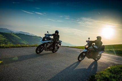 Zwei Motorradfahrer auf einem kurvigen Bergweg bei Sonnenuntergang