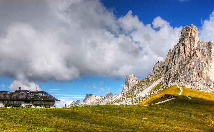 Südliche Dolomiten Haus vor grünen Hügeln und hohen Bergspitzen unter bewölktem Himmel