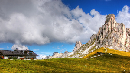 Haus vor grünen Hügeln und hohen Bergspitzen unter bewölktem Himmel
