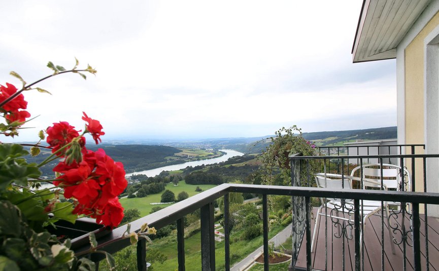 Balkon mit roten Blumen mit Blick auf Fluss und grüne Landschaft
