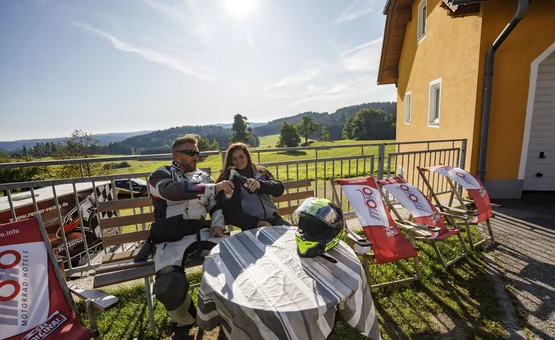Motorradfahrer genießen sonnige Pause mit Getränken auf Terrasse mit Bergblick