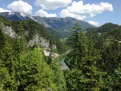 Blick auf bewaldete Berge und einen Fluss unter blauem Himmel mit Wolken