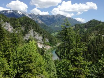 Blick auf bewaldete Berge und einen Fluss unter blauem Himmel mit Wolken