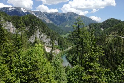 Blick auf bewaldete Berge und einen Fluss unter blauem Himmel mit Wolken