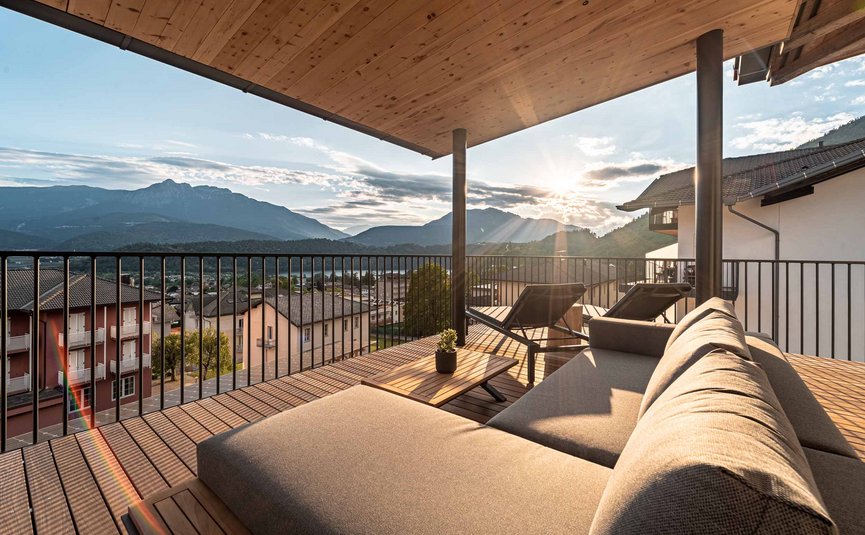 Balkon mit Sofa, zwei Liegestühlen und Bergpanorama bei Sonnenuntergang