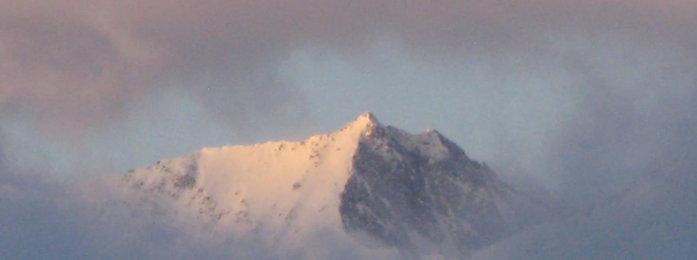 Schneebedeckter Berggipfel umgeben von Wolken bei Sonnenuntergang
