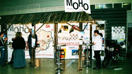 Messestand mit MoHo Motorradhotels in den Alpen und Besuchern