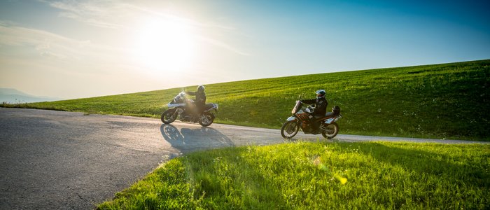 Mühlviertel © Moppetfoto.de Twee motorrijders op een landweg met groene heuvels en fel zonlicht