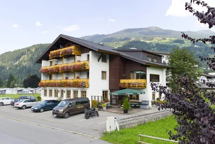 Hotelgebäude mit Balkonblumen und Bergen im Hintergrund