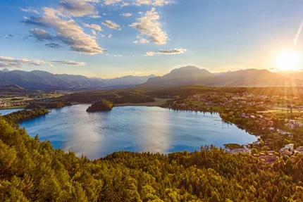 Lake surrounded by forest and mountains at sunset