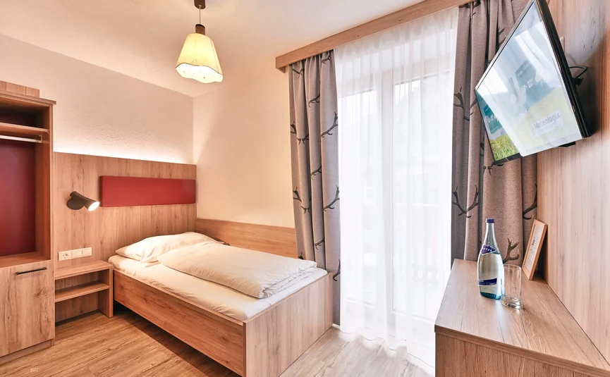 Small modern single room with bed, TV, and window with curtains