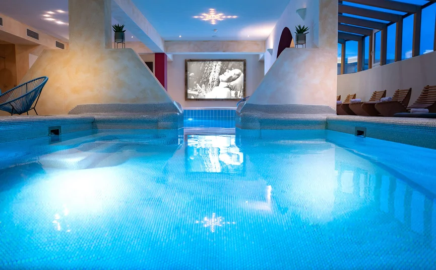 Indoor pool with blue water and lounge chairs in a spa area