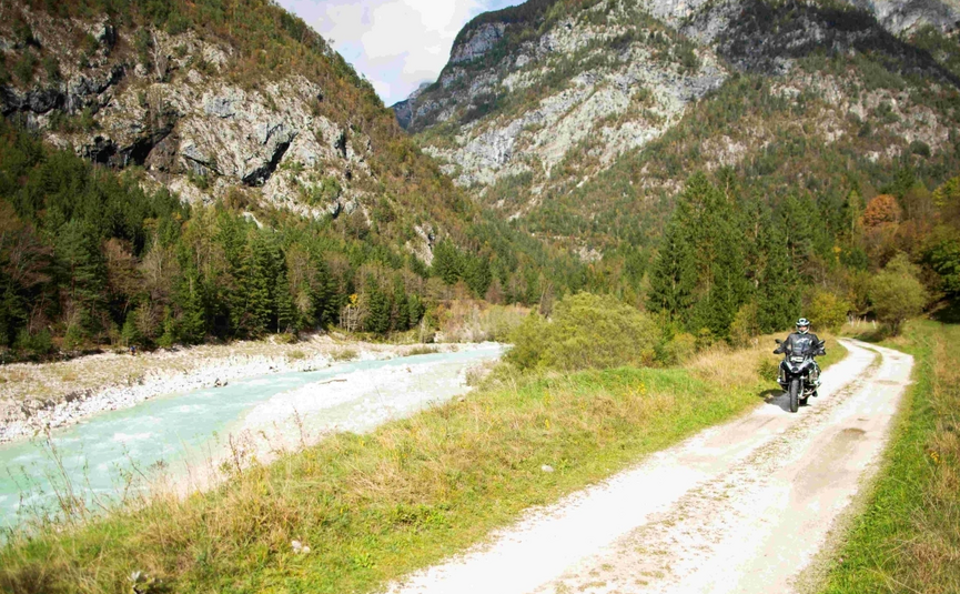 Emerald Soča River & Alpine Peaks Tour Motorcyclist on forest trail next to river in mountainous landscape
