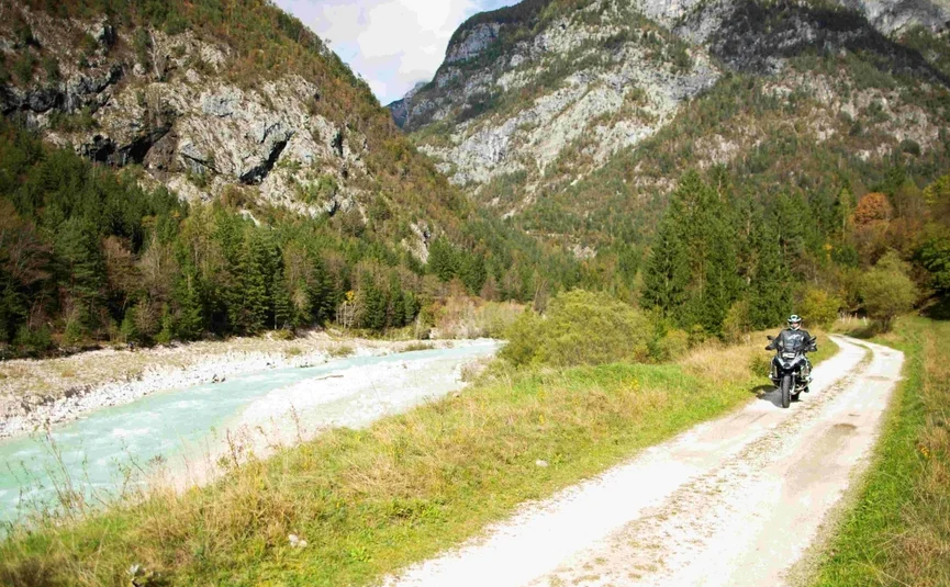 Motorradfahrer auf einem Waldweg neben einem Fluss in bergiger Landschaft