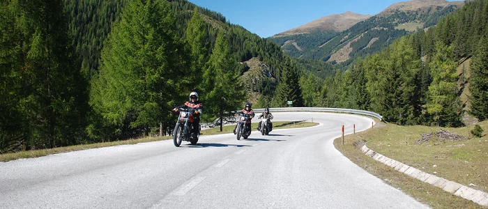 Three motorcyclists riding on a winding mountain road under clear sky