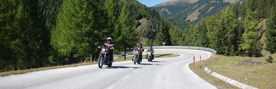 Motorradurlaub im Gailtal und den Karnischen Alpen © Hotel Gasthof Strasswirt Drei Motorradfahrer fahren auf kurviger Bergstraße bei klarem Himmel