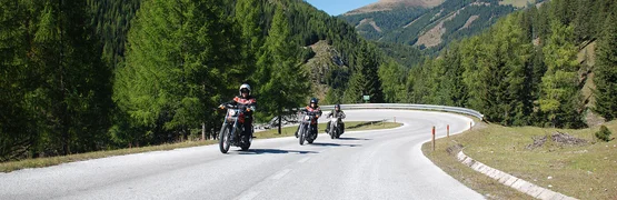 Drei Motorradfahrer fahren auf kurviger Bergstraße bei klarem Himmel
