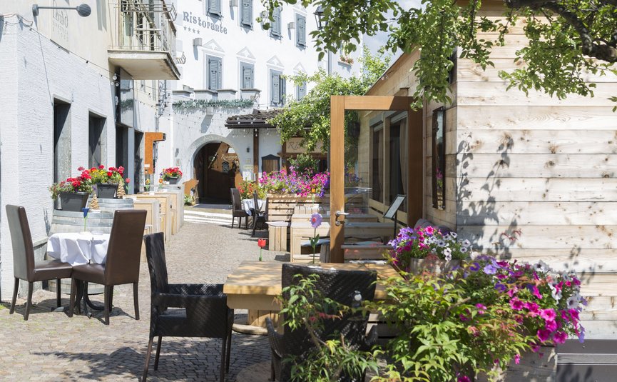Sonnige Straße mit Außensitzbereichen und bunten Blumen vor Restaurants
