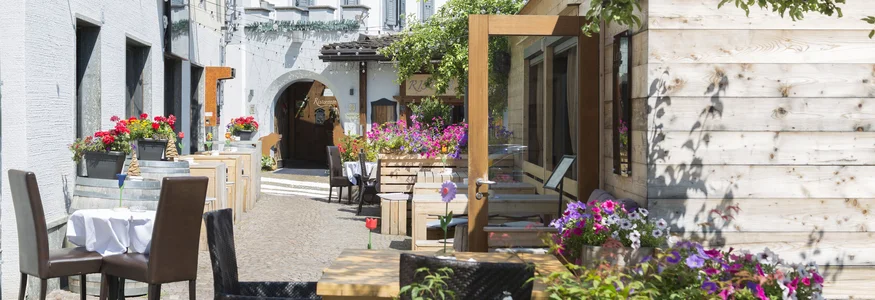 Hotel La Stüa **** © Hotel La Stüa Sonnige Straße mit Außensitzbereichen und bunten Blumen vor Restaurants