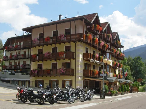 Multi-story hotel with flower balconies and motorcycles parked outside on sunny day
