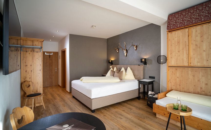 Gemütliches Hotelzimmer mit Doppelbett, Holzmöbeln und Hirschgeweihen an der Wand