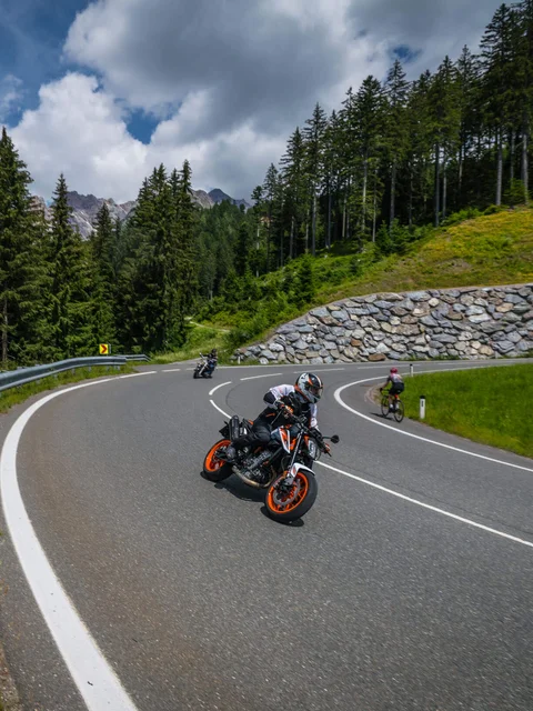 Motorcyclist on winding mountain road with cyclist and forest
