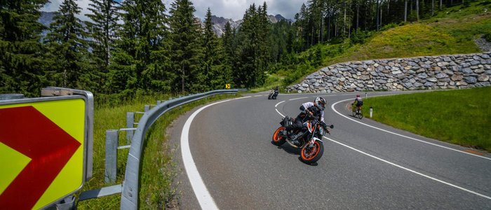 Motorradfahrer auf kurviger Bergstraße mit Fahrradfahrer und Wald