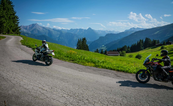 Zwei Motorradfahrer fahren auf Bergstraße mit Alpen im Hintergrund