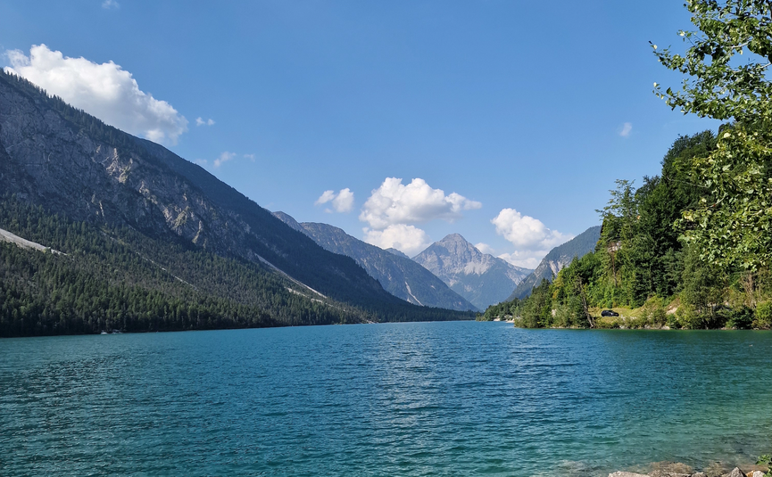 Klarer Bergsee mit Bergen, Wald und blauem Himmel