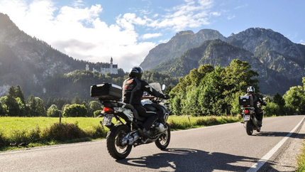 MoHo Schönauer Hof- Tour 7 Kulturtour Zwei Motorradfahrer fahren auf einer Bergstraße mit Schloss und Bergen im Hintergrund