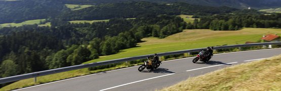 Motorradurlaub in der Region Rosenheim - Oberbayern © Jörg Künstle Zwei Motorradfahrer auf kurviger Bergstraße mit Bergen im Hintergrund