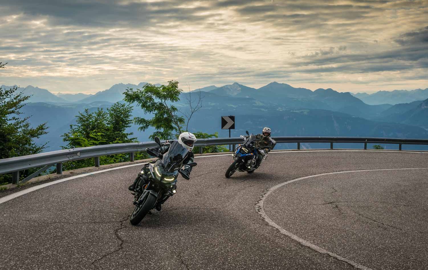 Urlaubsberater © Moppetfoto.de Zwei Motorradfahrer fahren auf einer kurvigen Bergstraße bei bewölktem Himmel