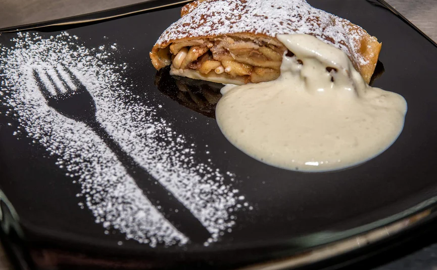 Appelstrudel met vanillesaus en poedersuiker op zwart bord