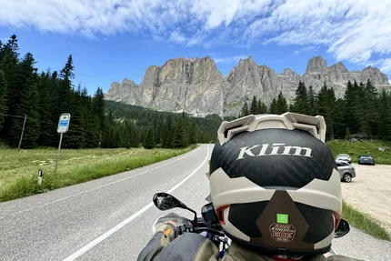 Motorcyclist riding on mountain road with pine trees and rocky mountains