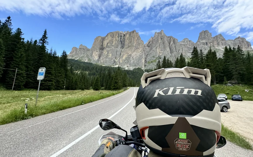 7th Lavaze - Val Gardena - Falzarego - Giau - www.ludwigshof.it Motorcyclist riding on mountain road with pine trees and rocky mountains