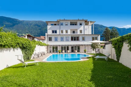 White house with swimming pool and garden in front of mountains under blue sky