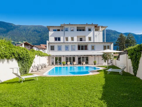 Weißes Haus mit Swimmingpool und Garten vor Bergen unter blauem Himmel