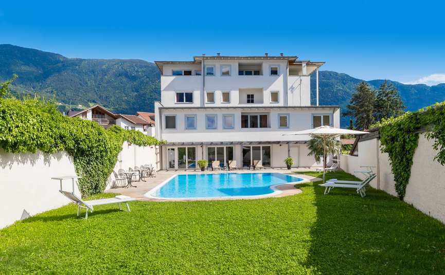 Weißes Haus mit Swimmingpool und Garten vor Bergen unter blauem Himmel