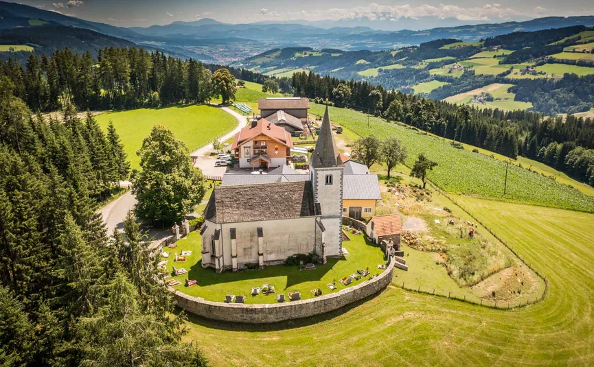 Church with cemetery on green hill surrounded by forests and mountains